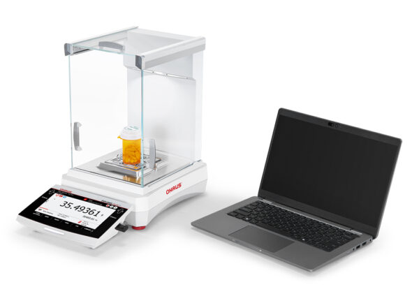 Explorer 2025 model Semi-Micro Balance Plus EXP being used with a laptop and orange liquid on the weighing pan, viewed side on, white background.