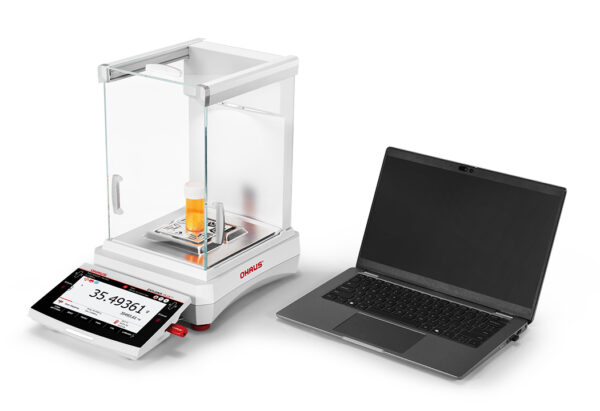 Explorer 2025 model Semi-Micro Balance Plus EXP being used with a laptop utilising the second USB slot and orange liquid on the weighing pan, viewed side on, white background.