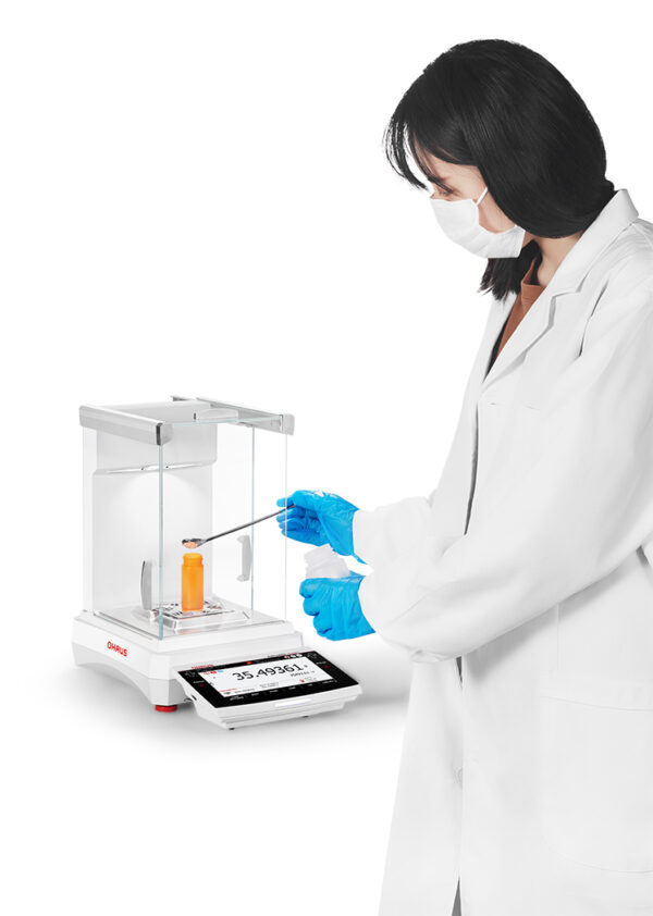 Ohaus Explorer, 2025 model, Semi-Micro Balance, Plus EXP, viewed from the side being used by someone measuring out a substance onto the balance. White background.